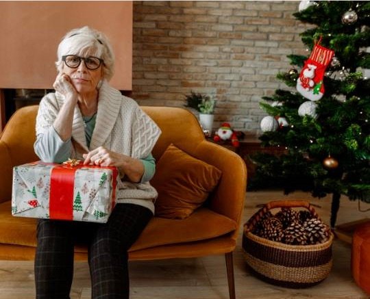idosa sentada sozinha na sala com presente de Natal no colo
