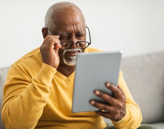 Idoso com dificuldades para enxergar texto no tablet