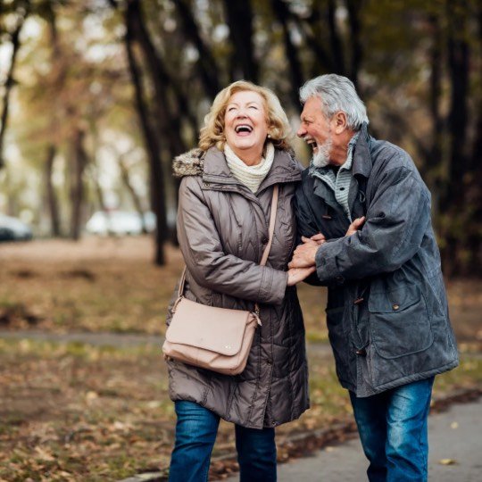Casal de idosos caminhando abraçados e felizes