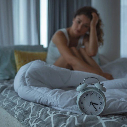 Mulher sentada na cama sem conseguir dormir