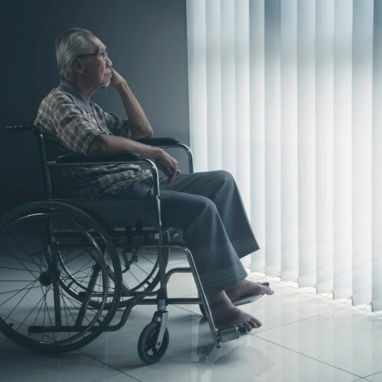 Idoso sentado em cadeira paraplégica pensando na janela