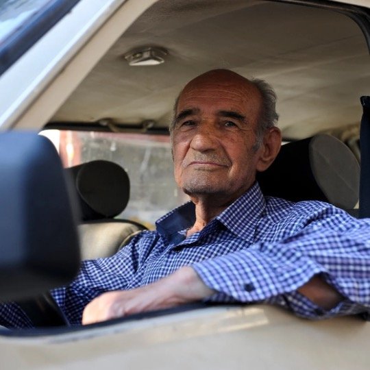 Homem idoso posando em frente ao volante do carro