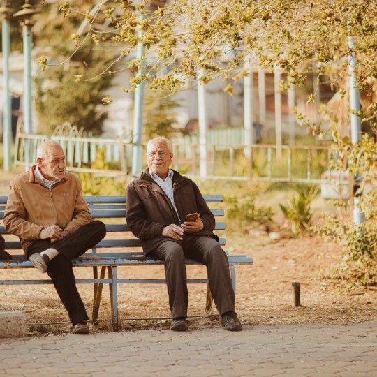 Dois idosos conversando em banco de praça